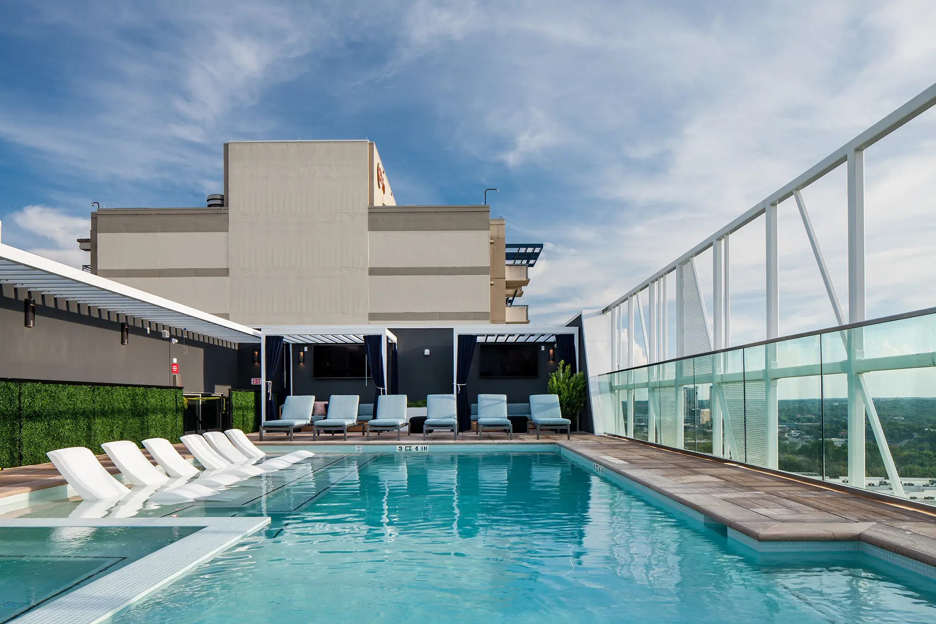 rooftop pool with lounge seating in shallow deck and pergola seating with large TVs.